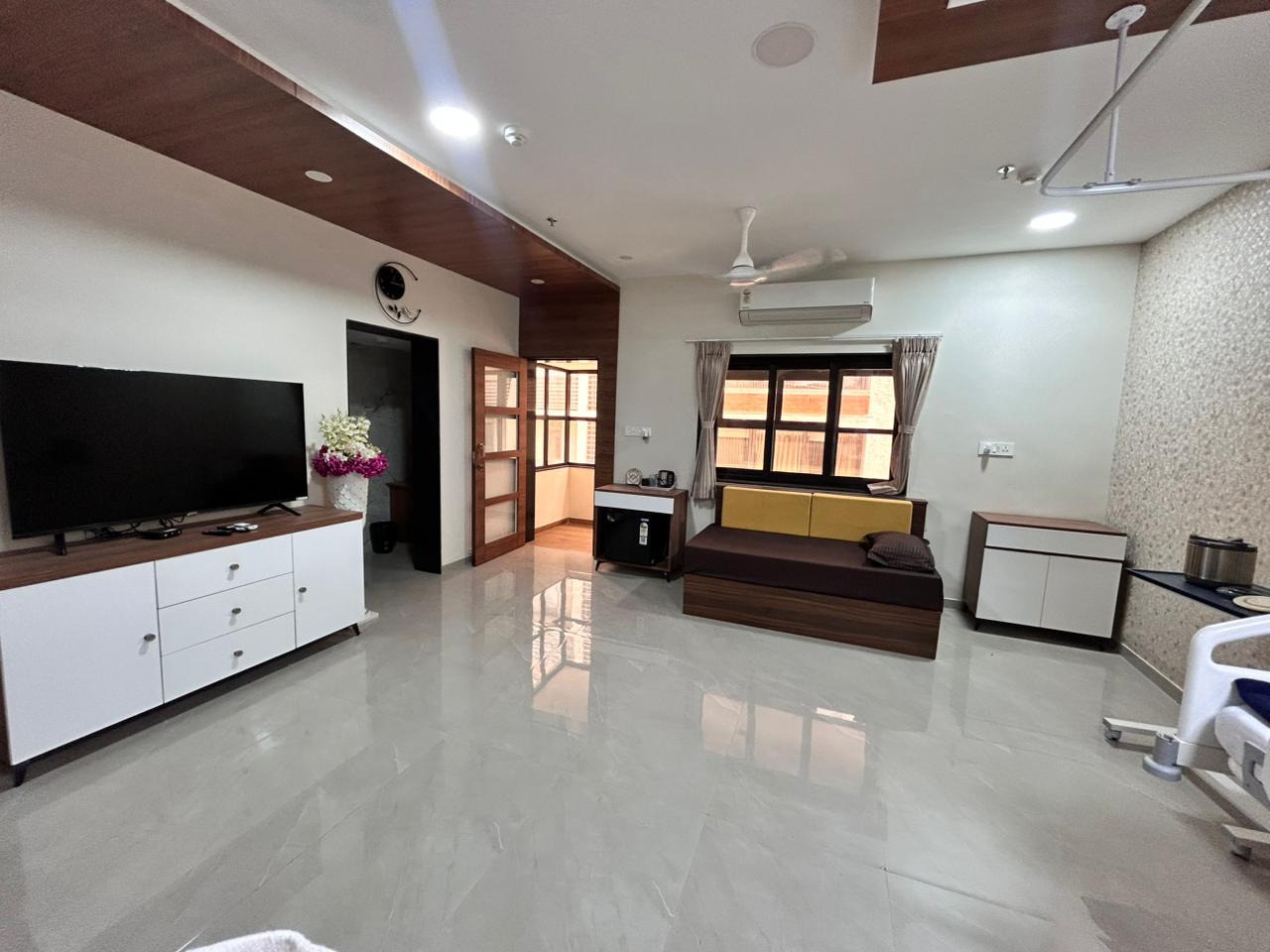 The patient room at Shah Hospital — well-lit interior with adjustable bed, attendant sofa, wallpapered accent wall and decorative ceiling.